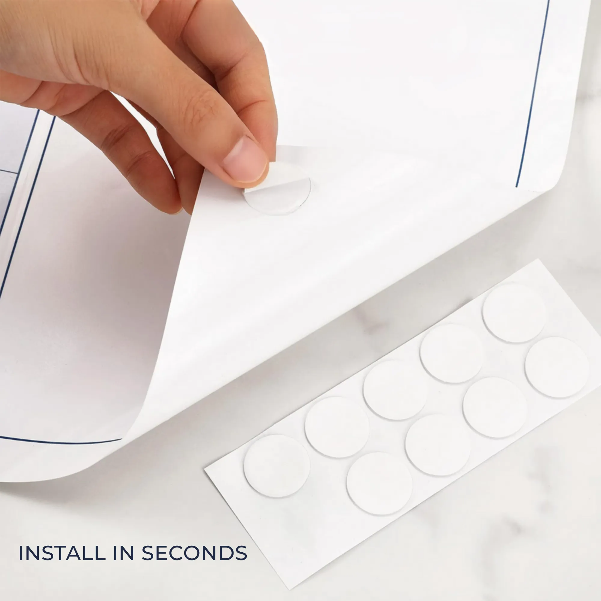 Peeling a no-drill adhesive mounting dot to hang the wall calendar
